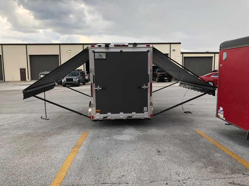 A warehouse parking lot with a trailer and two custom awnings extended
