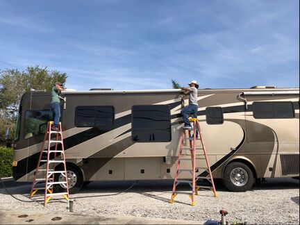 David Jones (Left) and John (right) perform an awning replacement on a RV underneath blue sky
