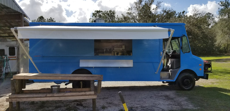 A blue food truck with an extended custom awning and picnic bench in front