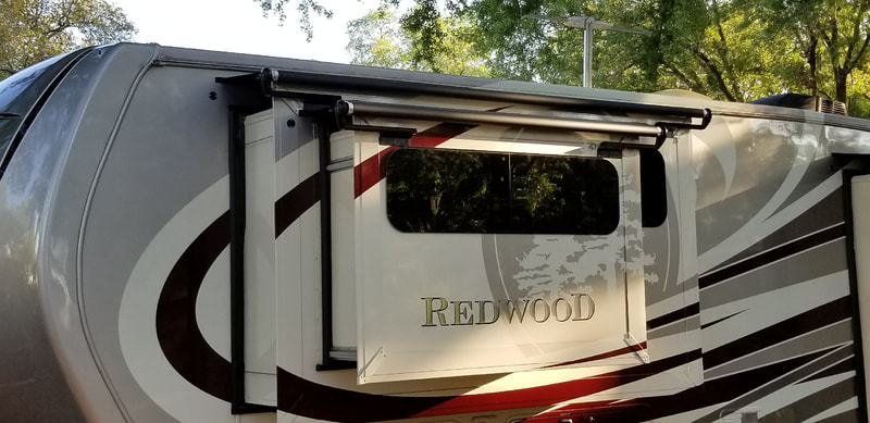 A red and tan RV with "Redwood" on the side and a custom awning