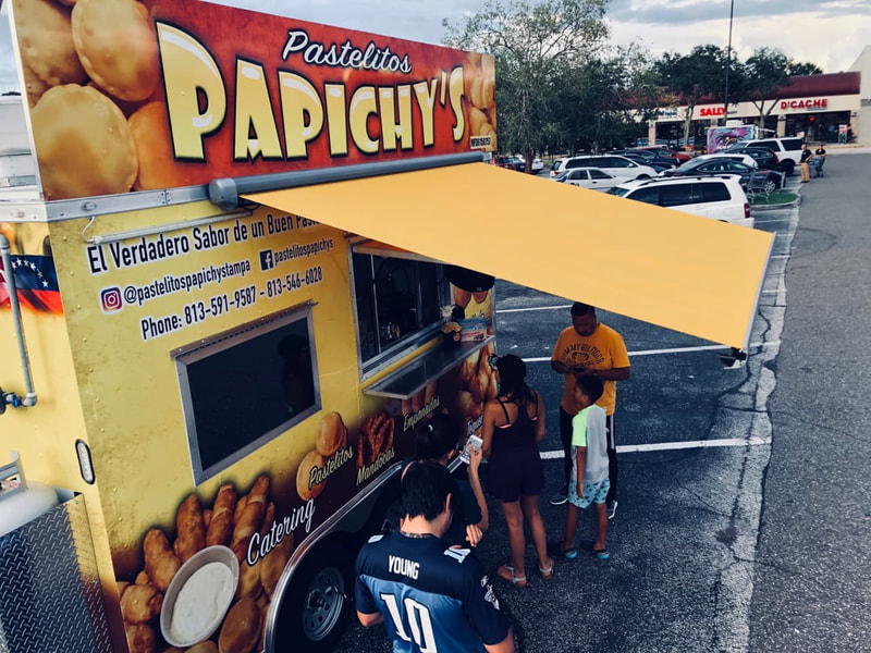 A parking lot with a yellow food stand called "Papichy's" and an extended yellow custom awning 