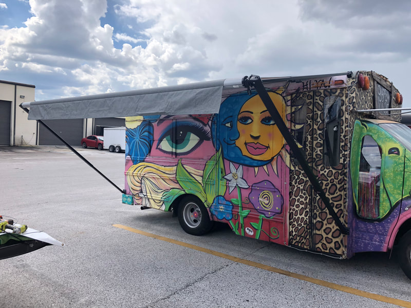 A colorful and artistic van in a parking lot with an extended custom awning