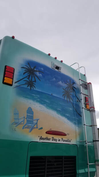 The back of an aquamarine RV with a painted beach and 