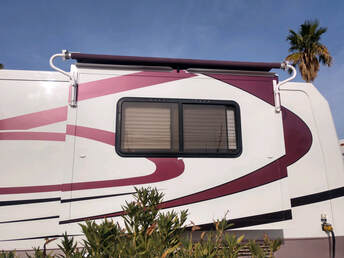 A white and red RV with a new awning and a palm tree in the background