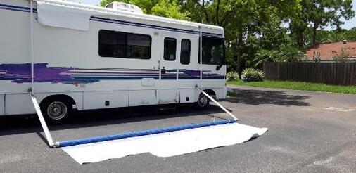 A blue and white RV with a broken awning that was ripped down