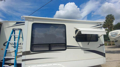 Blue sky and a RV with an extended window awning and a blue ladder