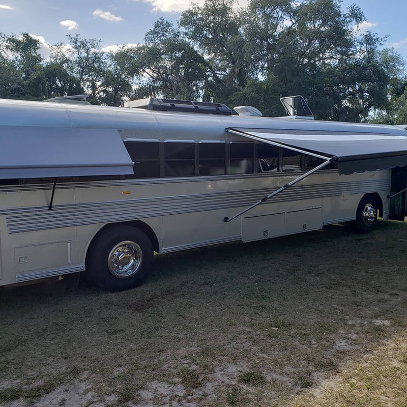 A silver bus with two extended custom awnings